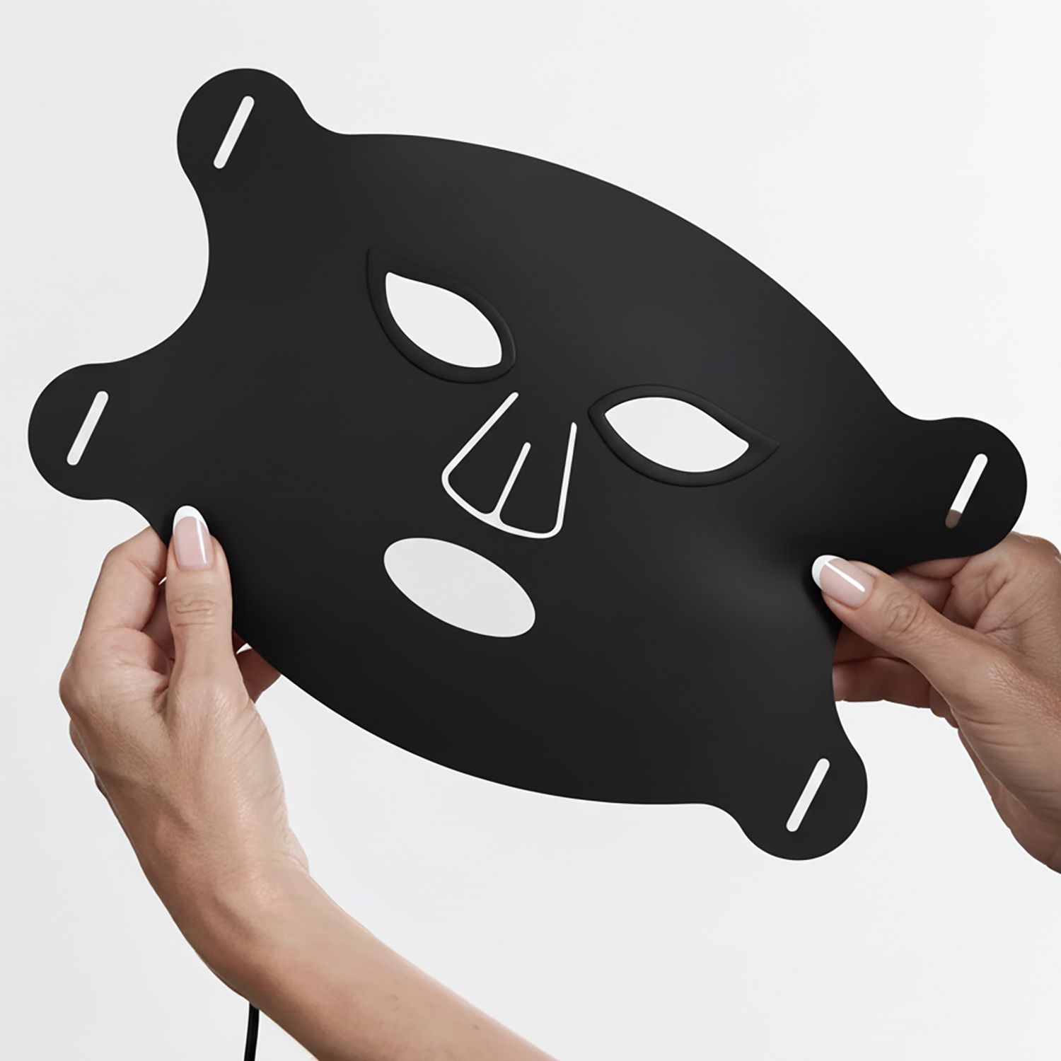 Für sichtbar glatter wirkende Haut Zwei Hände halten eine schwarze LED-Gesichtsmaske mit Aussparungen für Augen, Nase und Mund.